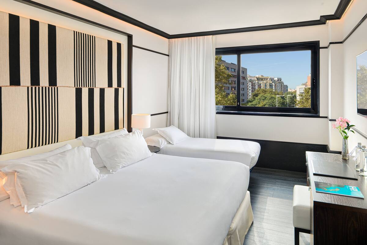 Ein Hotelzimmer mit zwei Betten, einem Schreibtisch und einem Fenster mit Blick auf die Stadt.