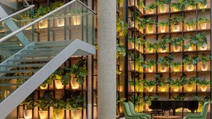 Un espacio interior moderno con una escalera, un piano, sillas verdes y una fuente de agua.