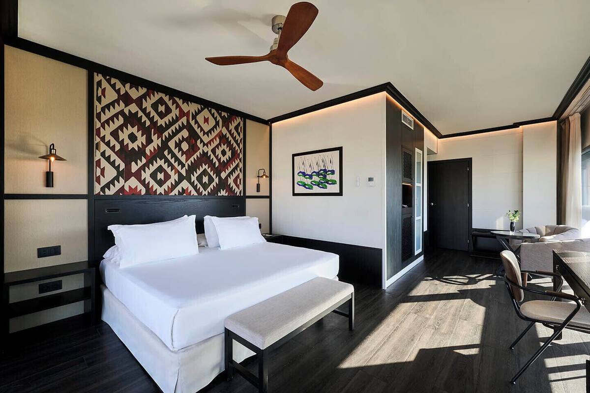 Ein modernes Hotelzimmer mit einem großen Bett, einem Schreibtisch und einem Deckenventilator.