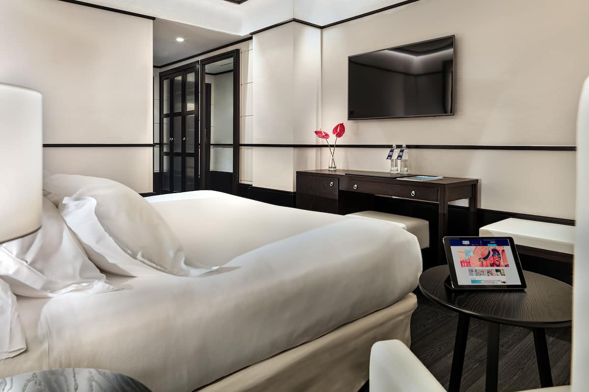 Una habitación de hotel con una cama grande, un escritorio con computadora, un televisor y una mesita.
