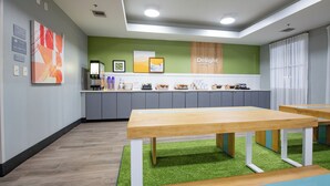 Un espacio de oficina moderno con una zona de recepción, una mesa con varios objetos y una pared verde con un letrero.