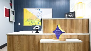 Un mostrador de recepción de hotel con diseño moderno, un cuadro abstracto grande en la pared, un letrero de 'Hilton Honors' y una placa de premio 'spark'.