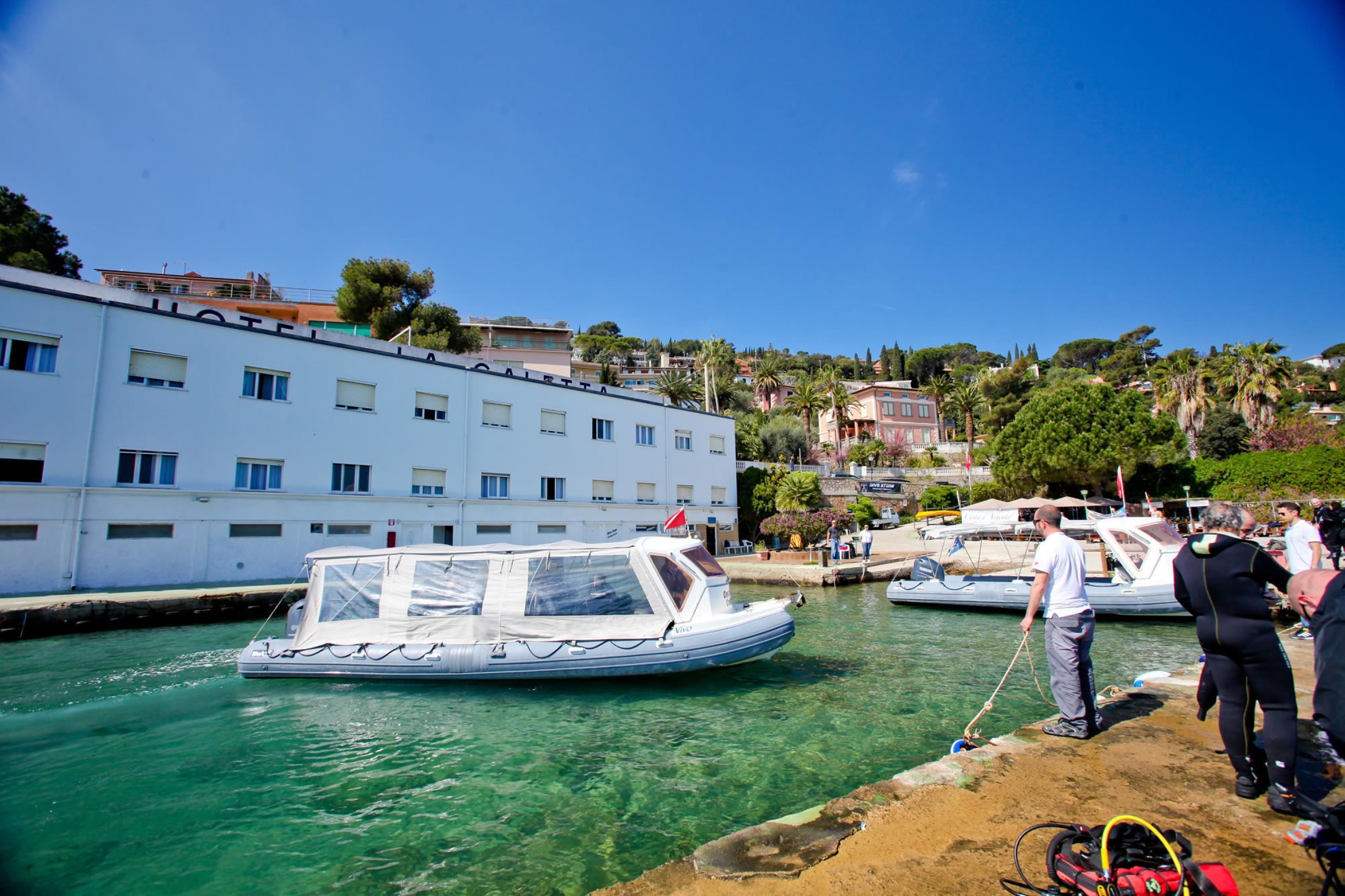 A marina with a white building, boats, and people near the water.