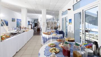 A buffet setup with various food items and beverages, a view of the sea through large windows, and a modern interior design.