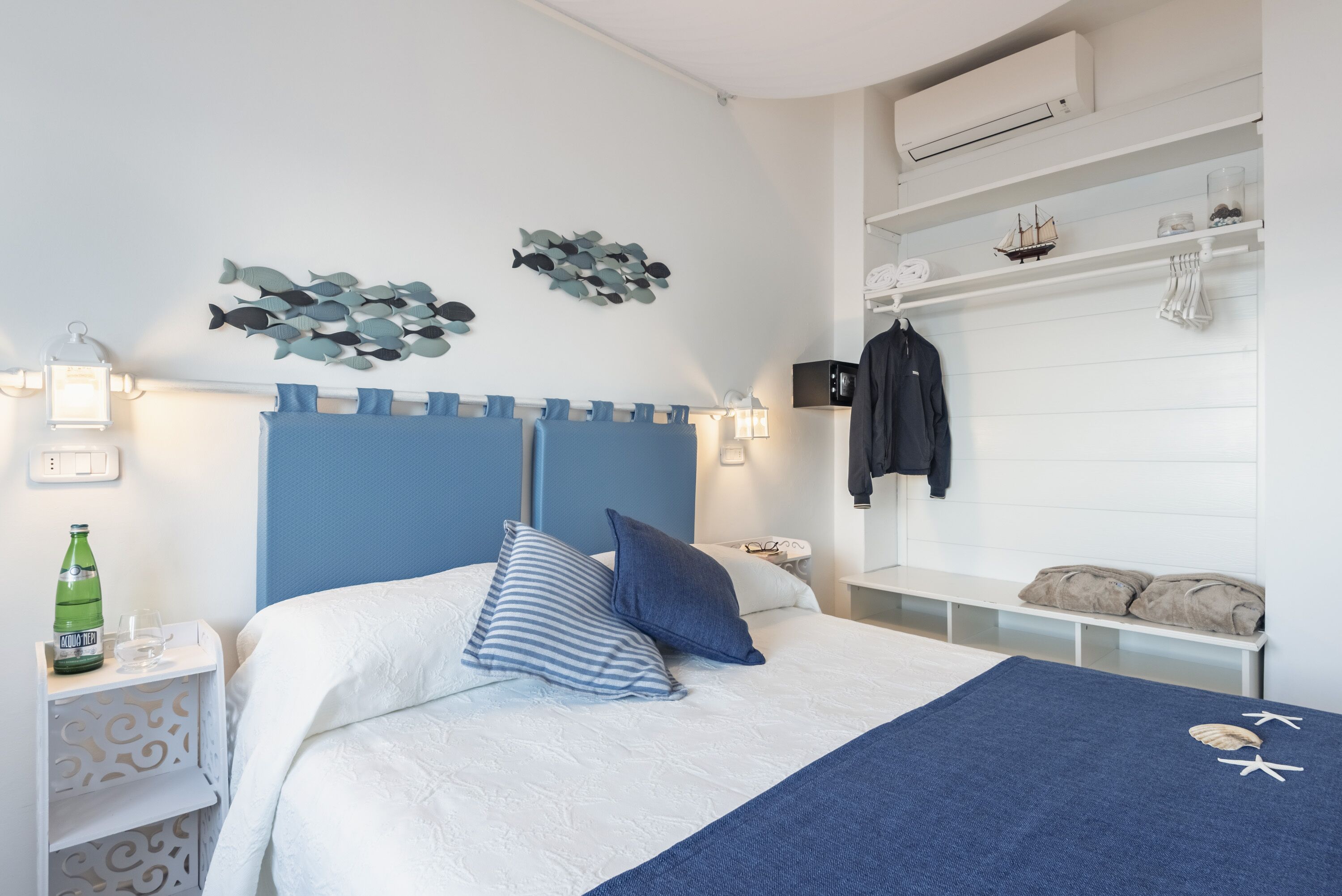 A neatly arranged bedroom with a bed, pillows, a nightstand, a shelf with decorative items, and a wall-mounted air conditioner.