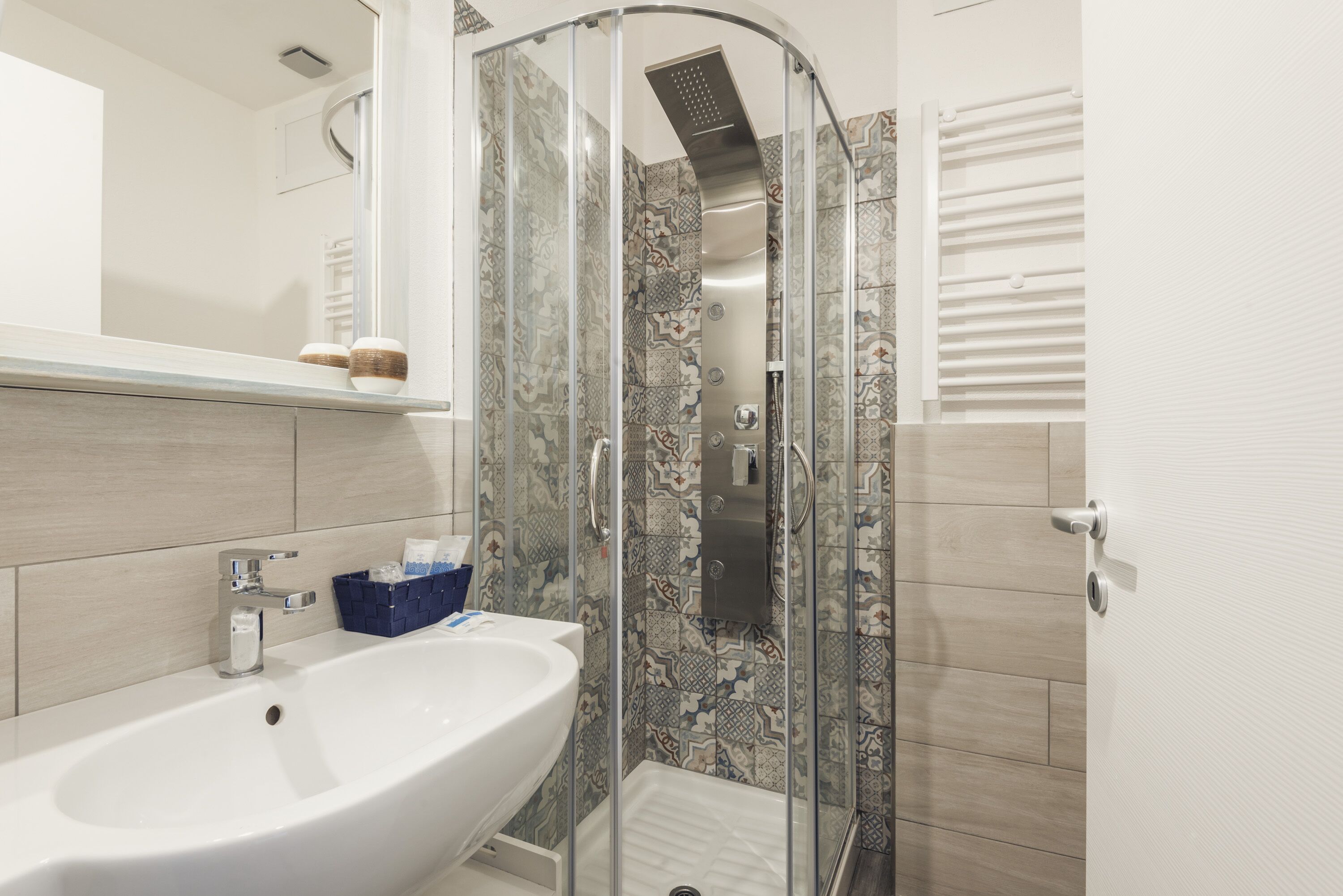 Un bagno moderno con cabina doccia in vetro, lavandino bianco e piastrelle decorate.