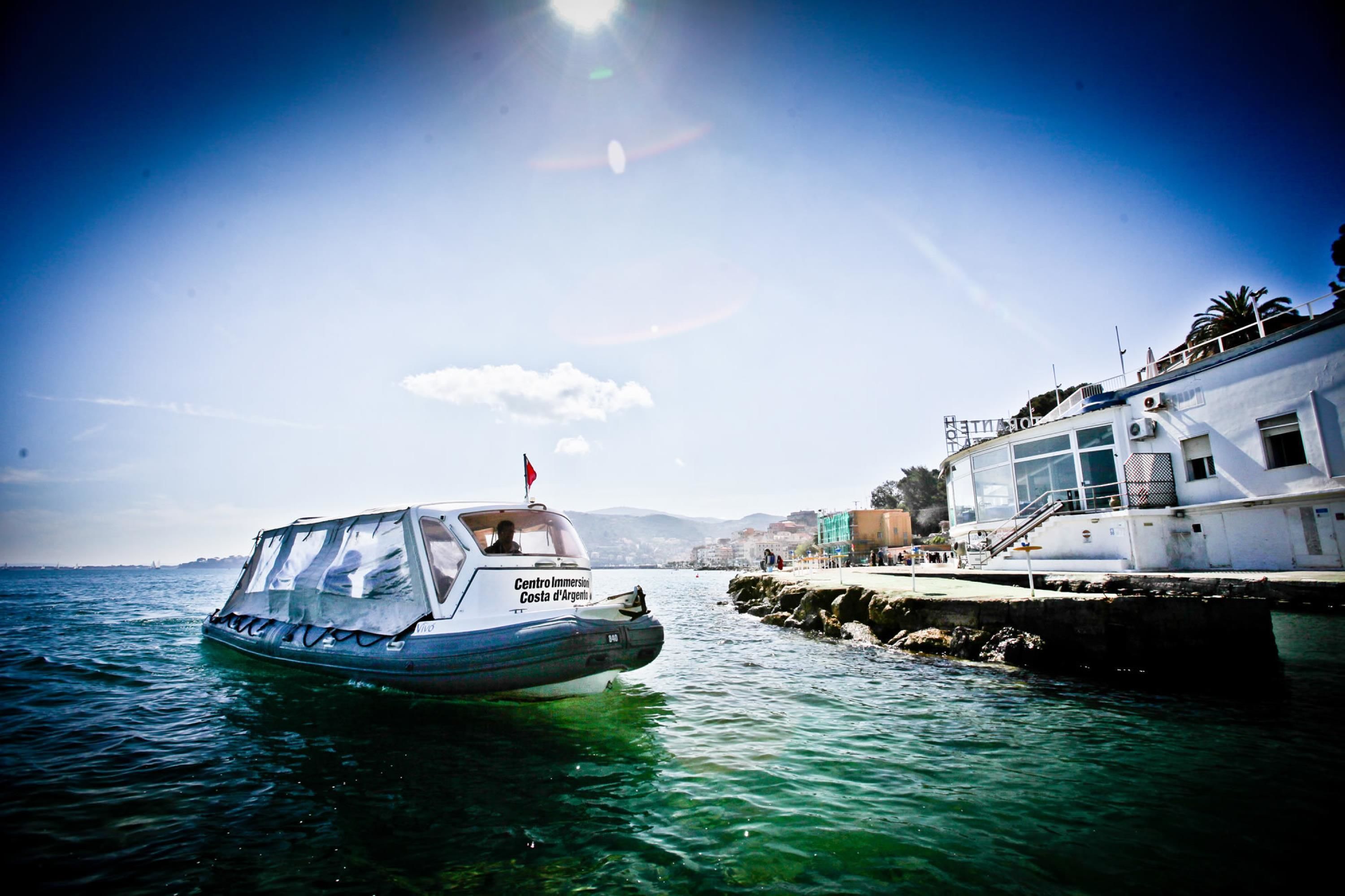 A boat named Centro Immersion Costa d'Argento docked at a pier with a white building nearby.