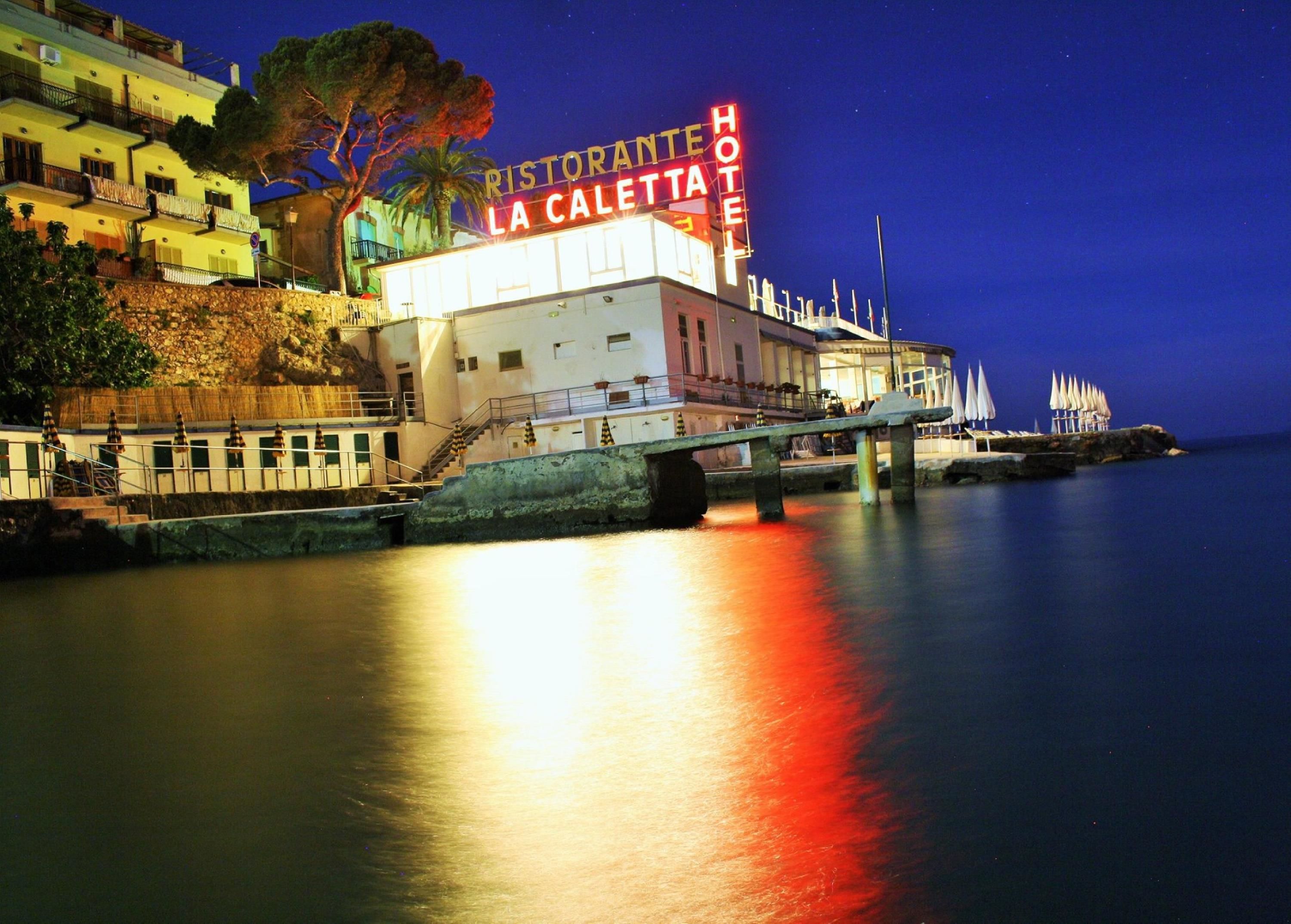 Un hôtel situé au bord de l’eau, avec une enseigne bien visible indiquant : « Ristorante La Caletta Hotel ».
