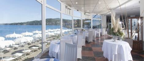 A restaurant with tables set for dining, large windows with a view of the sea and hills, and a checkered floor.