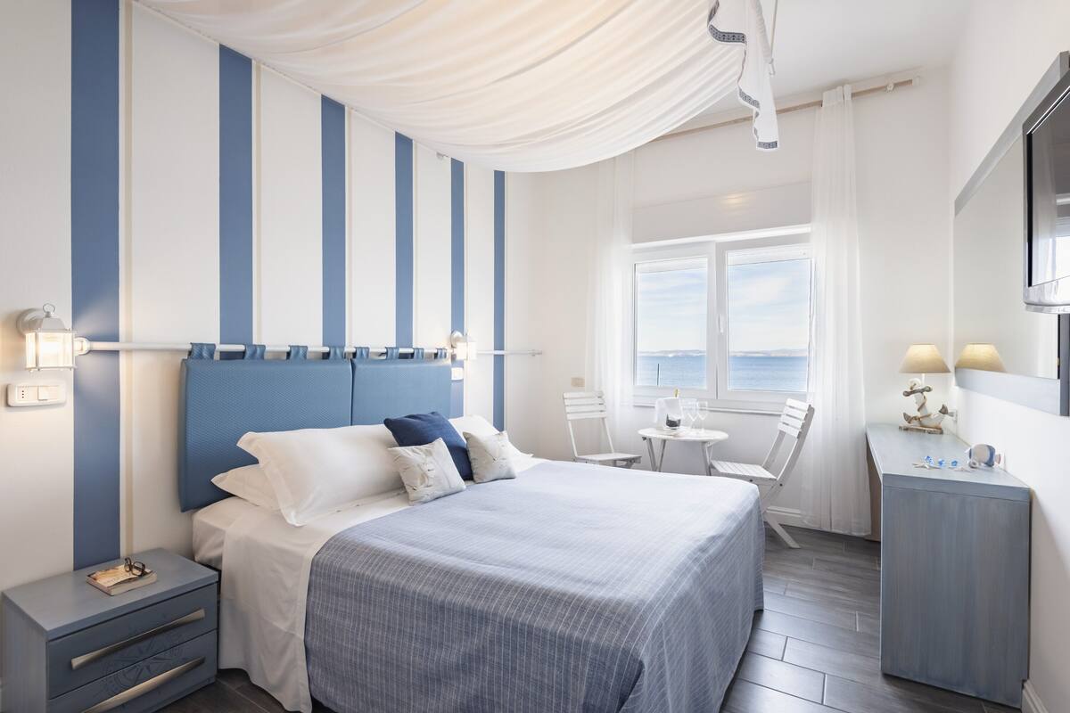 A hotel room with a large bed, a desk, and a view of the sea.