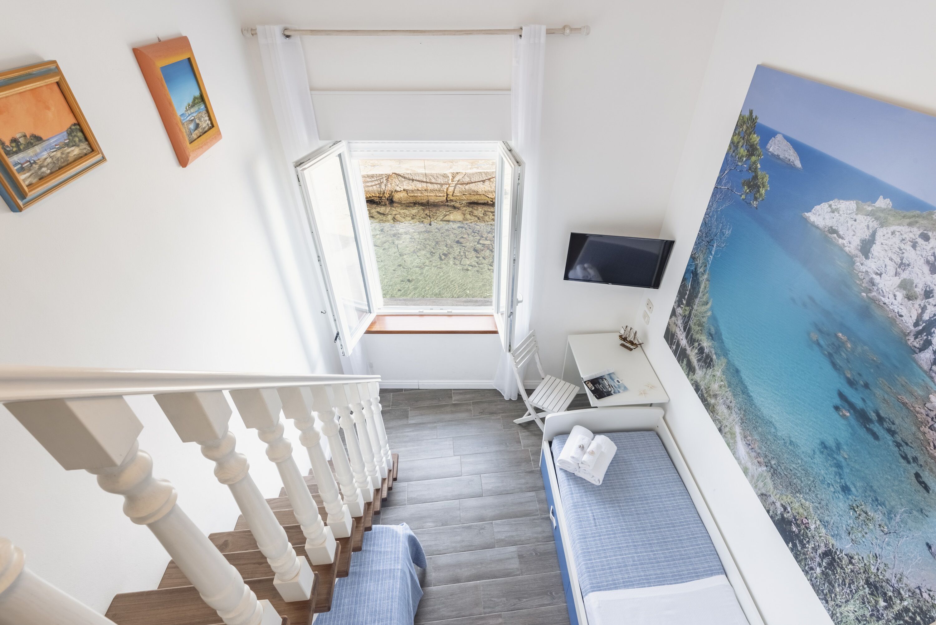 A room with a bed, a desk, a TV, and a large window with a view of a landscape.