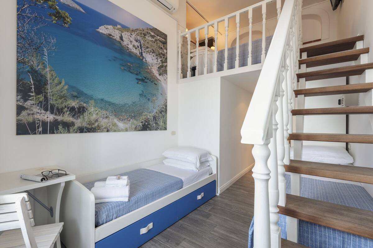 A bedroom with a bed, a desk, and a painting of a coastal landscape.