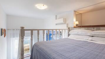 A bedroom with a bed, a window with a view of the sea, a ceiling light, and a wall-mounted air conditioner.