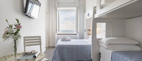 Habitación de hotel compacta con literas, una cama individual, una mesita con un florero y un televisor montado en la pared.