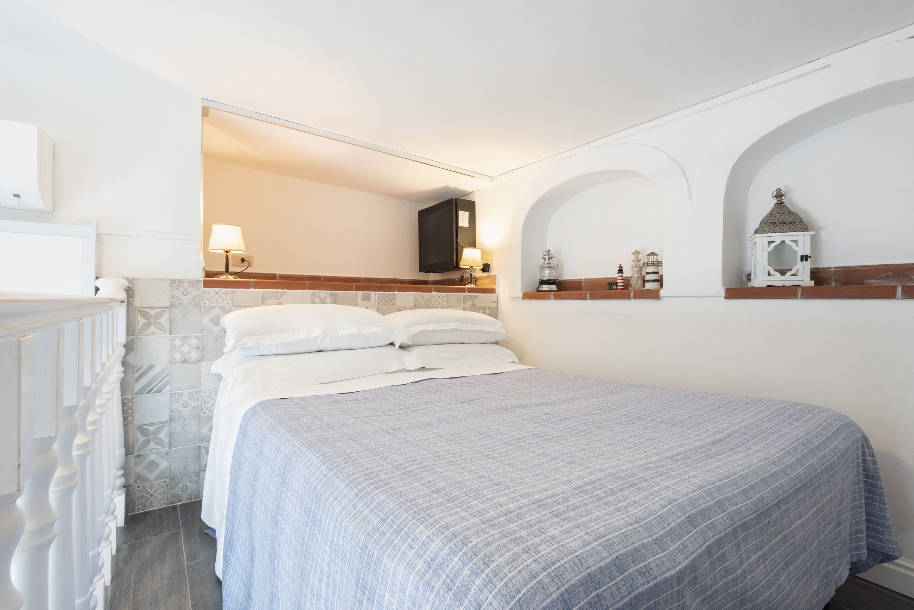 Un lit bien fait, recouvert d’une couvre-lit à rayures bleues et blanches, avec une tête de lit blanche et une petite table de chevet sur laquelle se trouve une lampe.