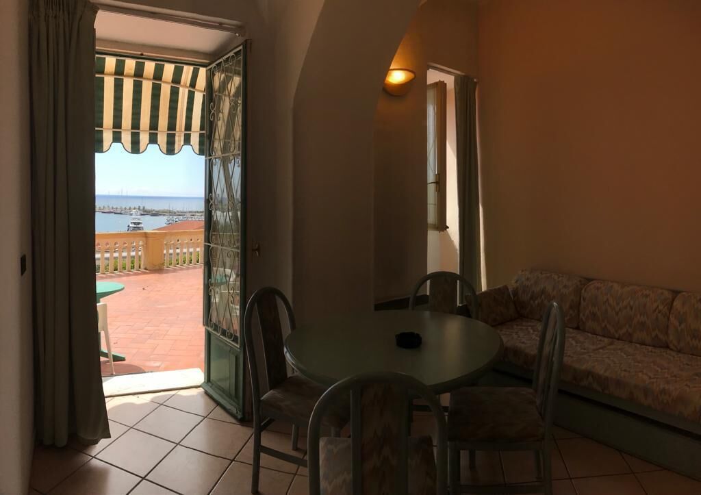 Una stanza con un balcone, un tavolo rotondo con sedie e un divano.