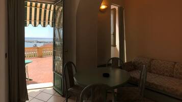 Una stanza con un balcone, un tavolo rotondo con sedie e un divano.