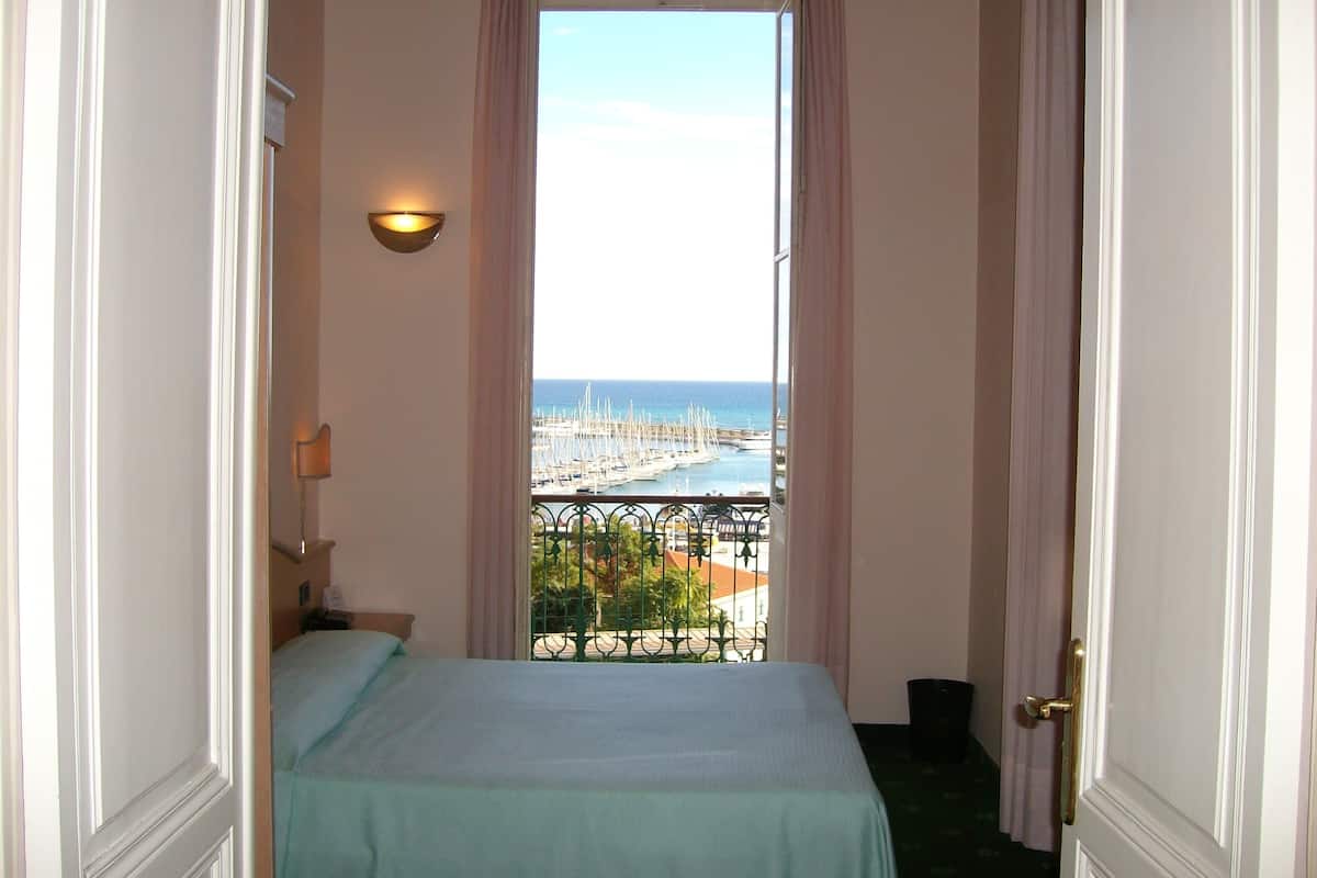 Una habitación pequeña con cama, una ventana con cortinas y vistas a un puerto deportivo.