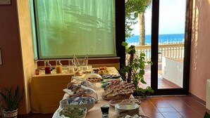 Una mesa de buffet con diferentes platillos, una ventana con vista al mar y una puerta que da al exterior.