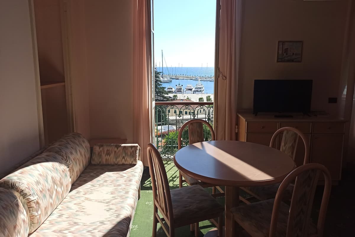 Un balcón con sofá y mesa de comedor, con vistas a un puerto deportivo lleno de barcos.