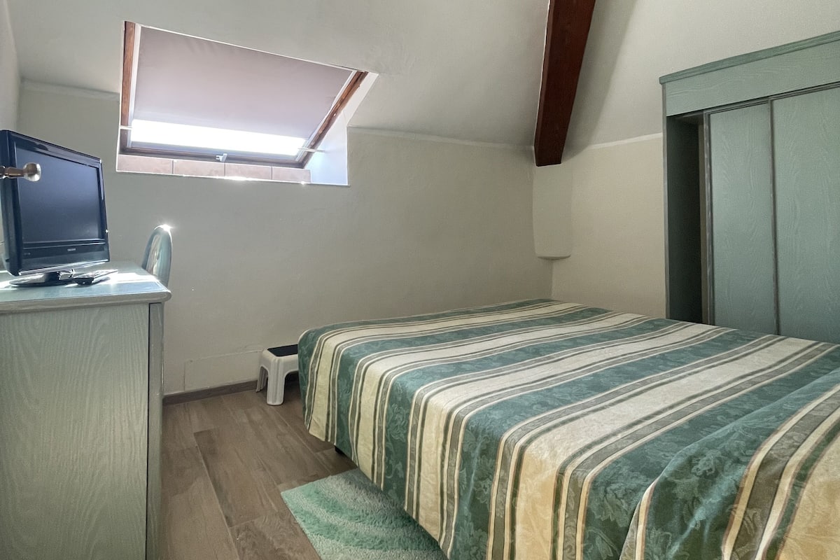 Un alojamiento pequeño de una sola habitación con escritorio, cama, ventana y techo inclinado.