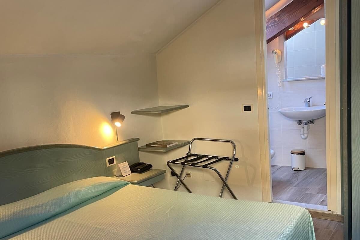 Un dormitorio con dos camas, una mesita de noche con lámpara, un tendedero y un estante pequeño.