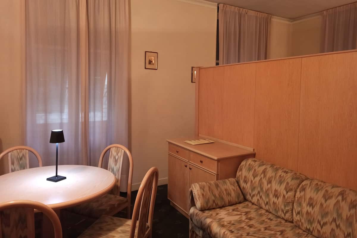 Una habitación con una mesa redonda, dos sillas, un sofá, un armario y una lámpara.