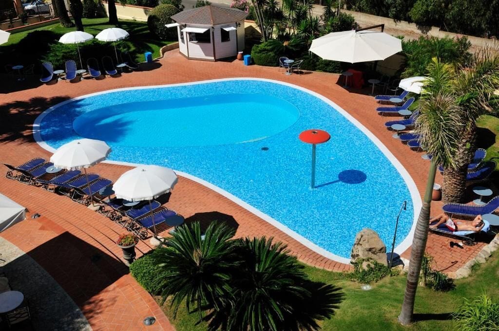 A swimming pool with lounge chairs and umbrellas, surrounded by palm trees and a small gazebo.