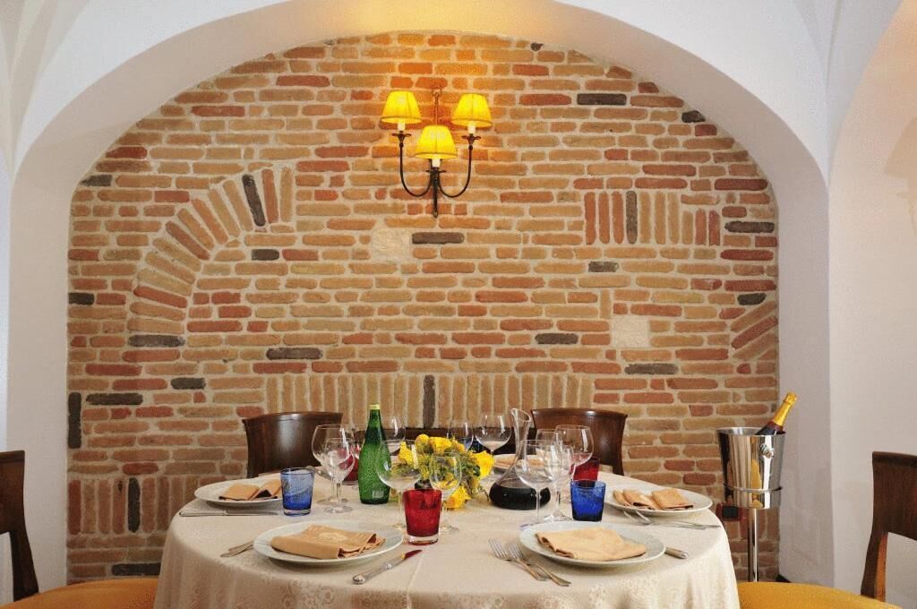 Een eettafel gedekt voor twee personen, met een bakstenen muur op de achtergrond, een kroonluchter en een fles champagne.