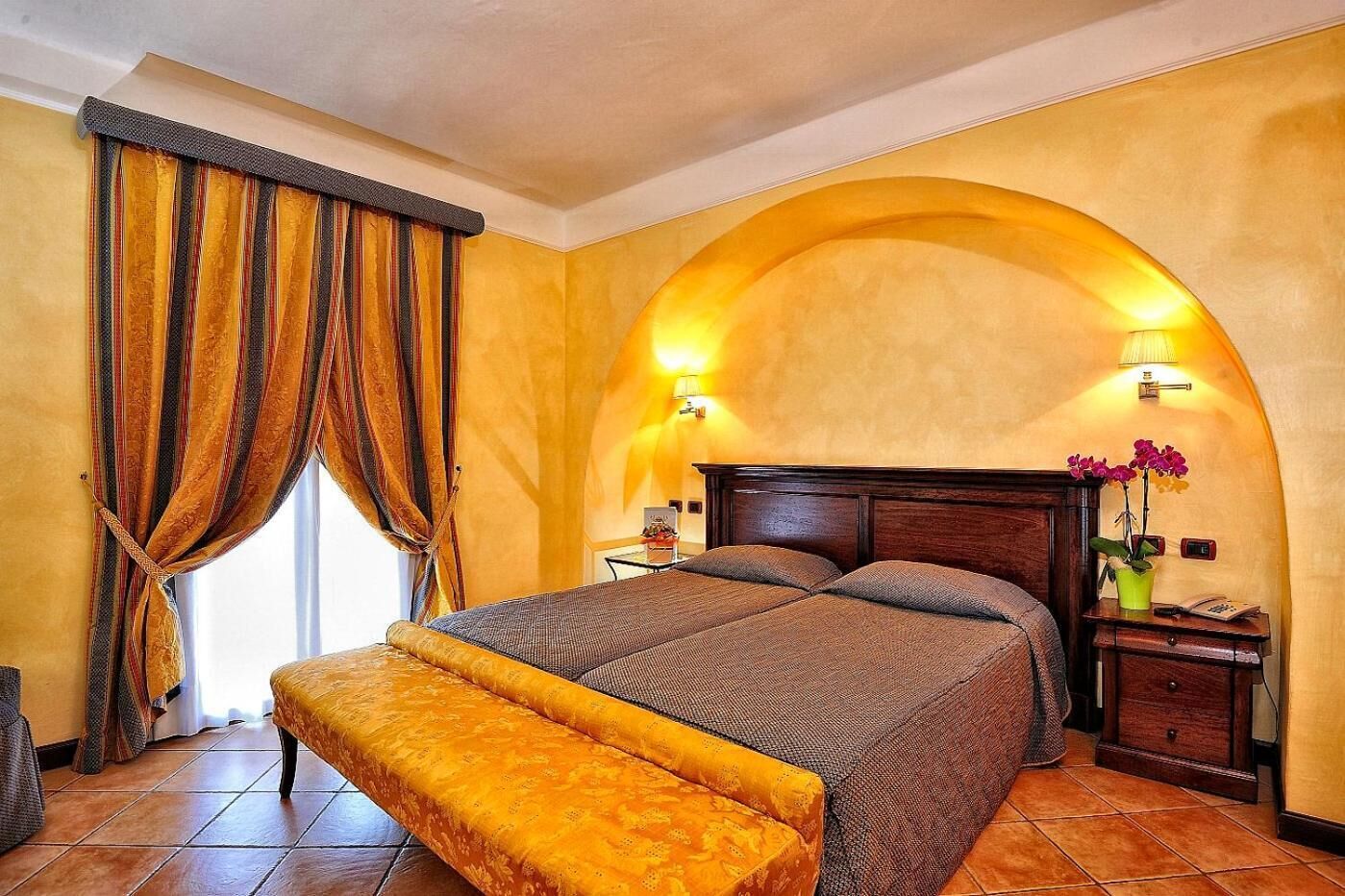 A bedroom with a large bed, a bench, a nightstand, and a wall-mounted lamp.