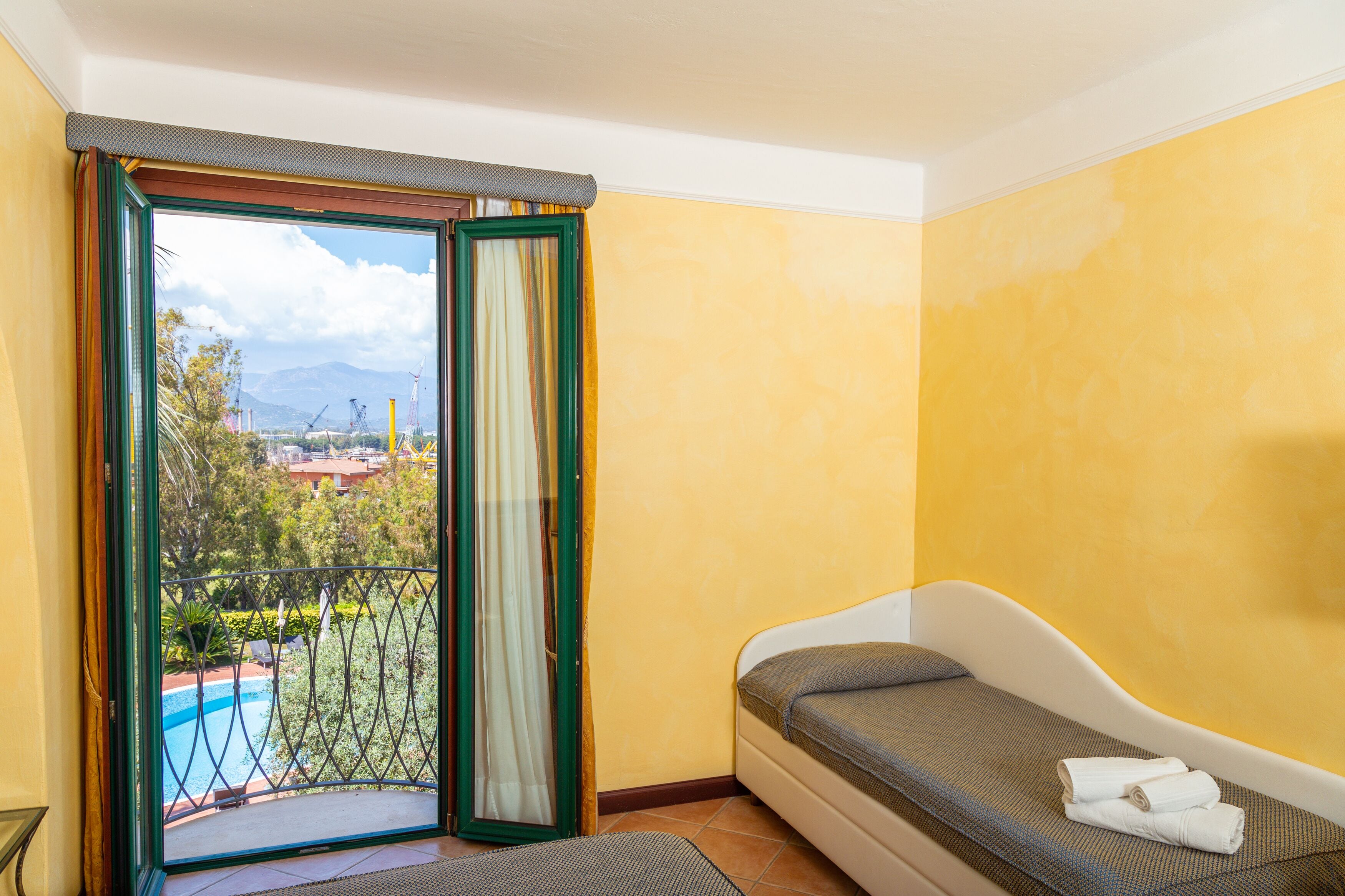 Une chambre avec balcon, un lit et vue sur une piscine et des montagnes.