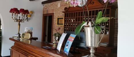 A reception desk with a wooden finish, a clock, and a metal vase with orchids.