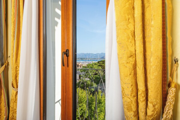 Una ventana con cortinas, vista de un paisaje urbano y montañas al fondo.