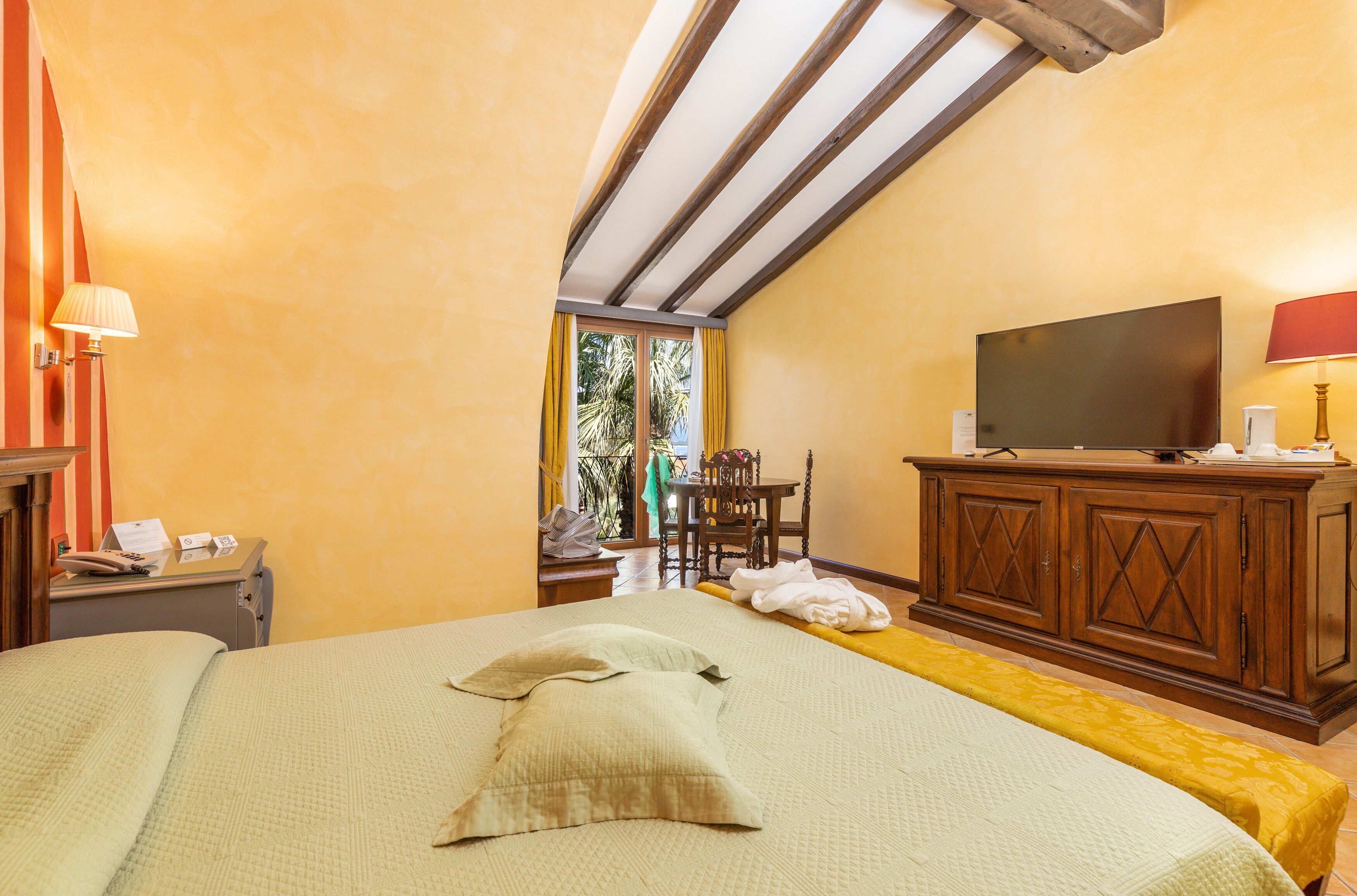 Una habitación de hotel con cama, televisor, aparador de madera y ventana con cortinas.