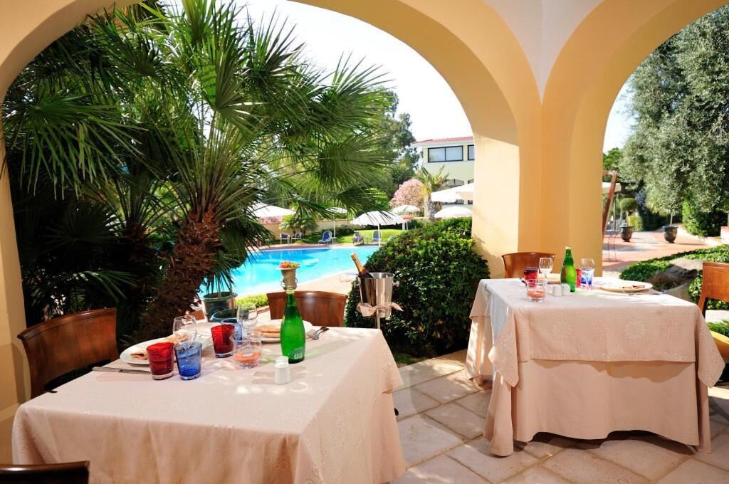 An outdoor dining area with tables set for two, overlooking a swimming pool and lush greenery.