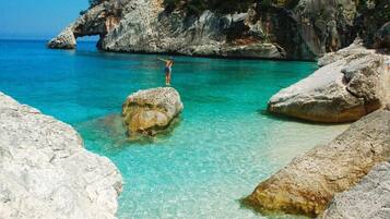 A rocky coastal scene with clear turquoise water and a person standing on a rock.