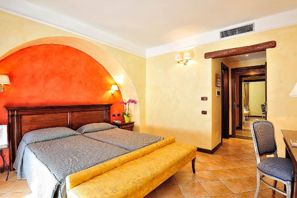 A hotel room with a bed, a bench, a desk, and a chair.