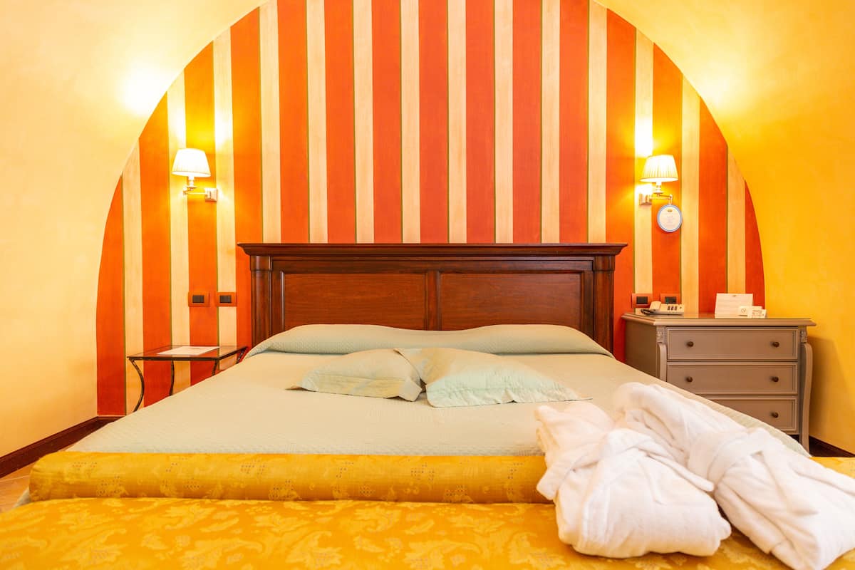 A hotel room with a large bed, two bedside lamps, a nightstand, and a wooden headboard.