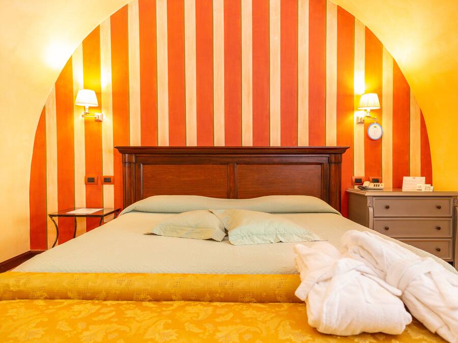 A hotel room with a large bed, two bedside lamps, a nightstand, and a wooden headboard.