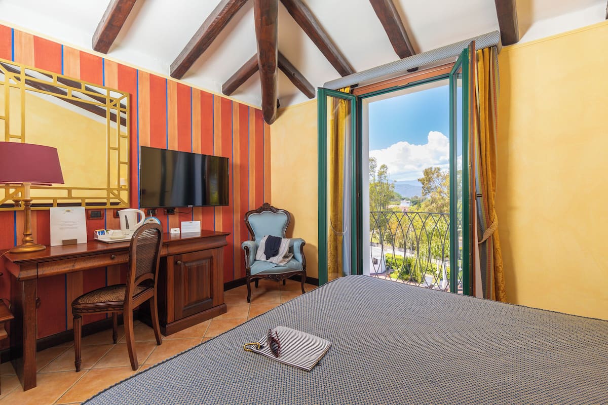 A hotel room with a bed, desk, chair, TV, and a balcony with a view.