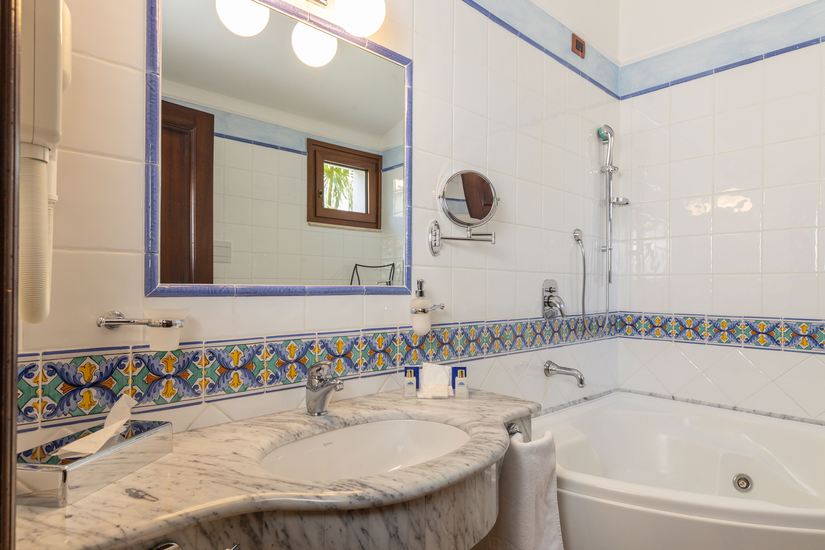 A bathroom with a large mirror, a bathtub, and a sink with a marble countertop.