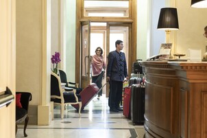 Hall d'albergo con reception, area relax con una poltrona e una persona con i bagagli.