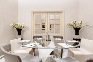 Una sala conferenze moderna con un tavolo in vetro, sedie bianche e due vasi di fiori bianchi.