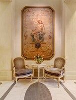 Una stanza con due poltrone imbottite, un tavolino con un vaso di fiori e un grande quadro decorativo appeso al muro.