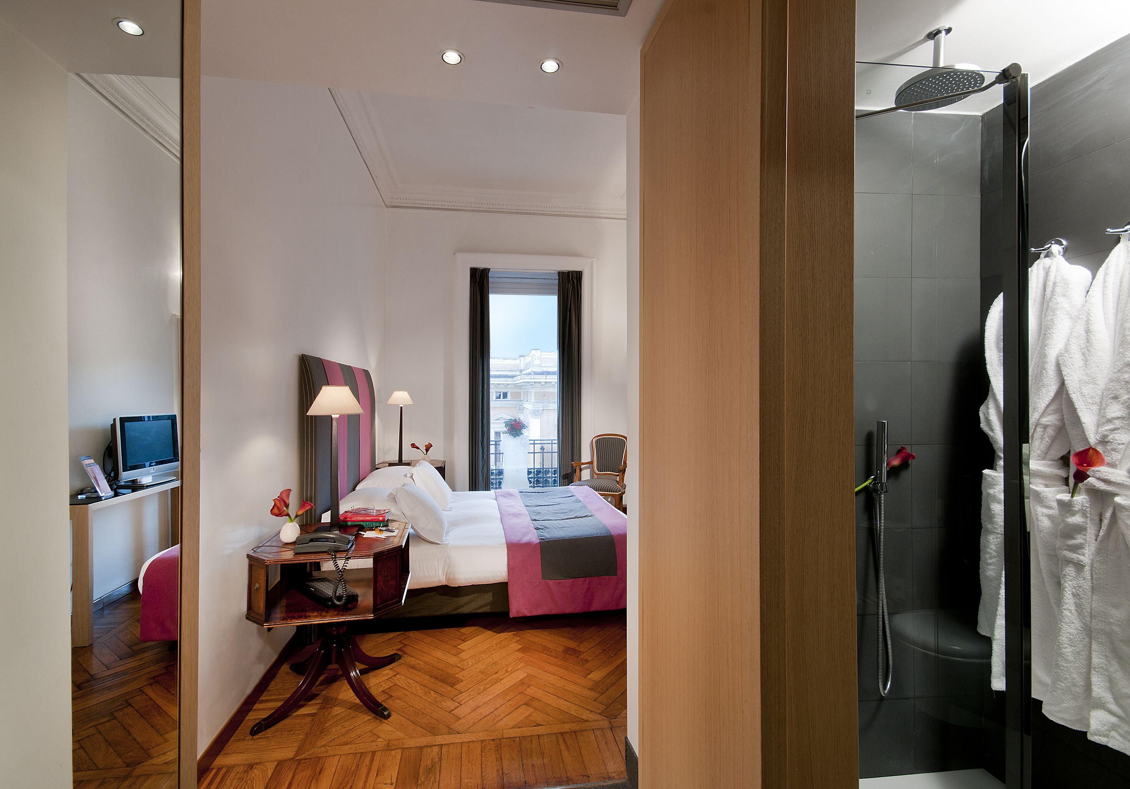 A hotel room with a bed, desk, computer, and a shower area.