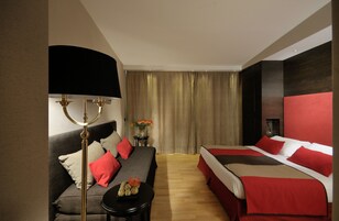 Una camera d'albergo con un divano, due letti singoli, un tavolo rotondo con una lampada e un tavolino con dei fiori.