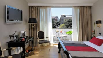Ein Hotelzimmer mit Bett, Schreibtisch mit Lampe, Stuhl, Fernseher und Balkon mit Tisch und Stühlen.