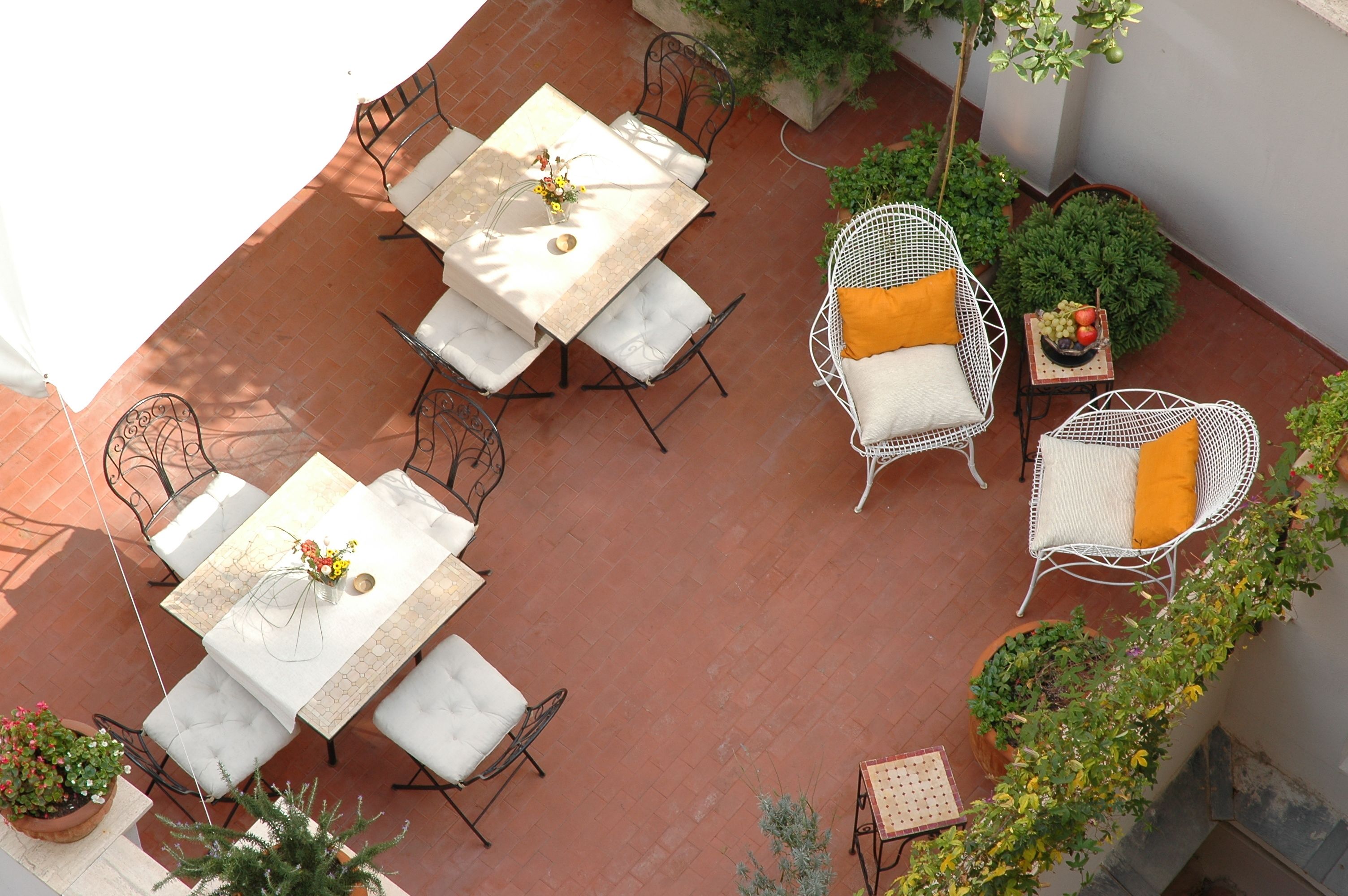 An outdoor patio with a table and chairs, surrounded by potted plants and a small table with fruit.
