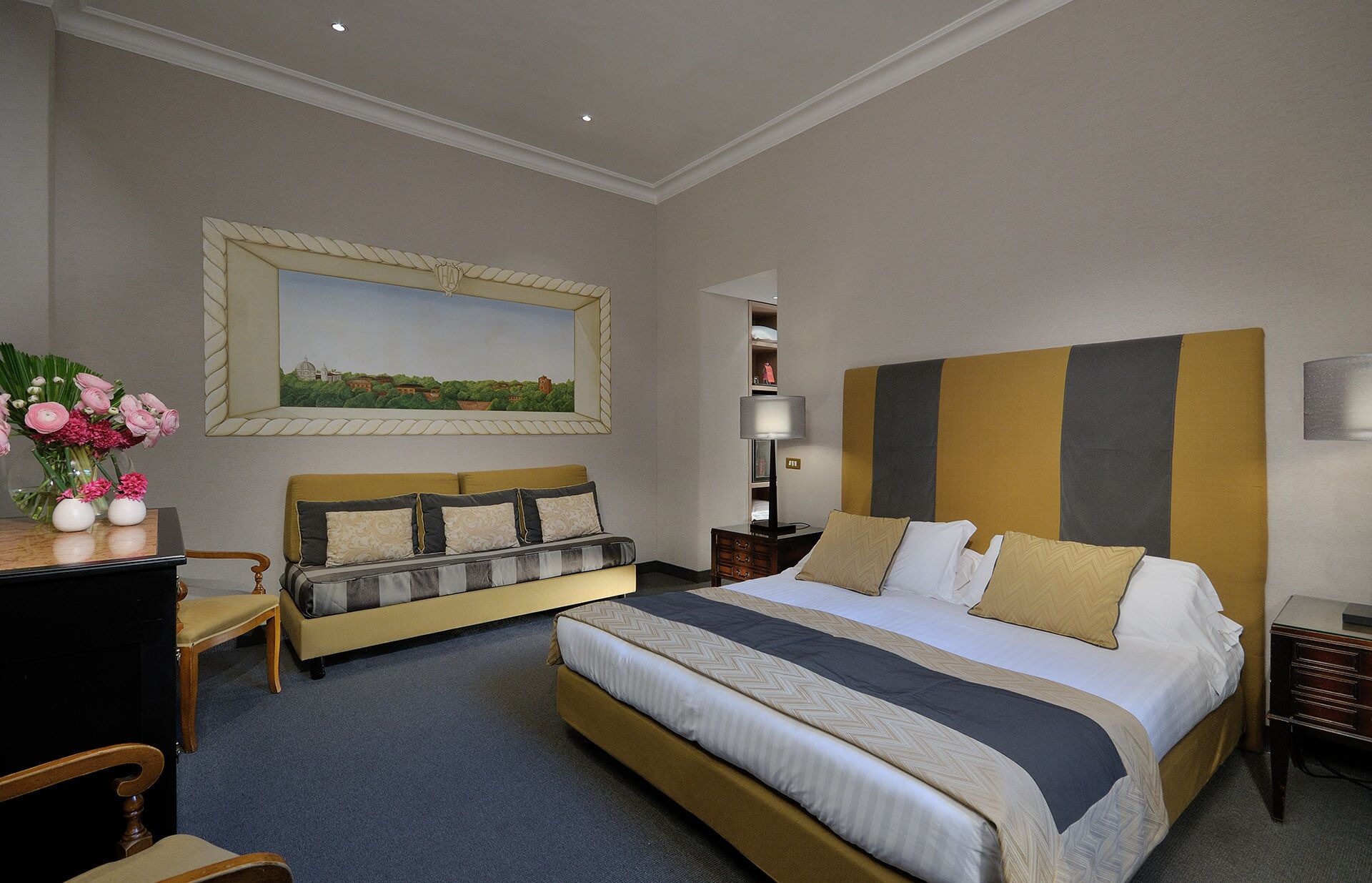 A hotel room with a large bed, a sofa, a desk, and a painting on the wall.