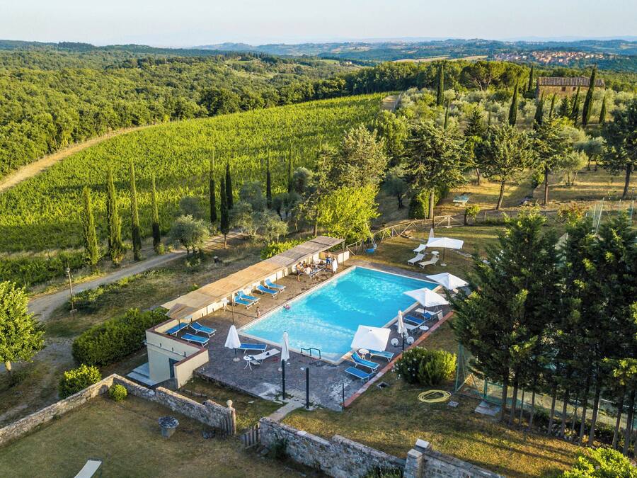 An aerial view of a villa with a swimming pool, surrounded by lush greenery and a hilly landscape.